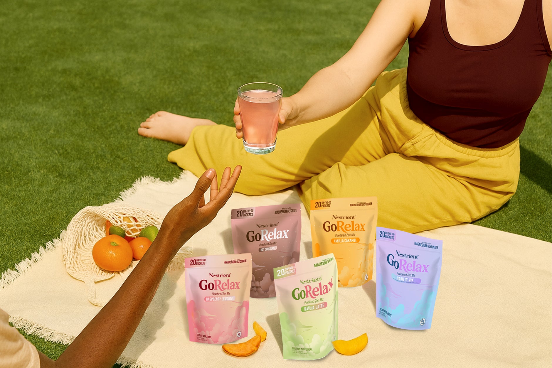 Person sitting on grass with a glass of pink drink, surrounded by GoRelax supplement packets.