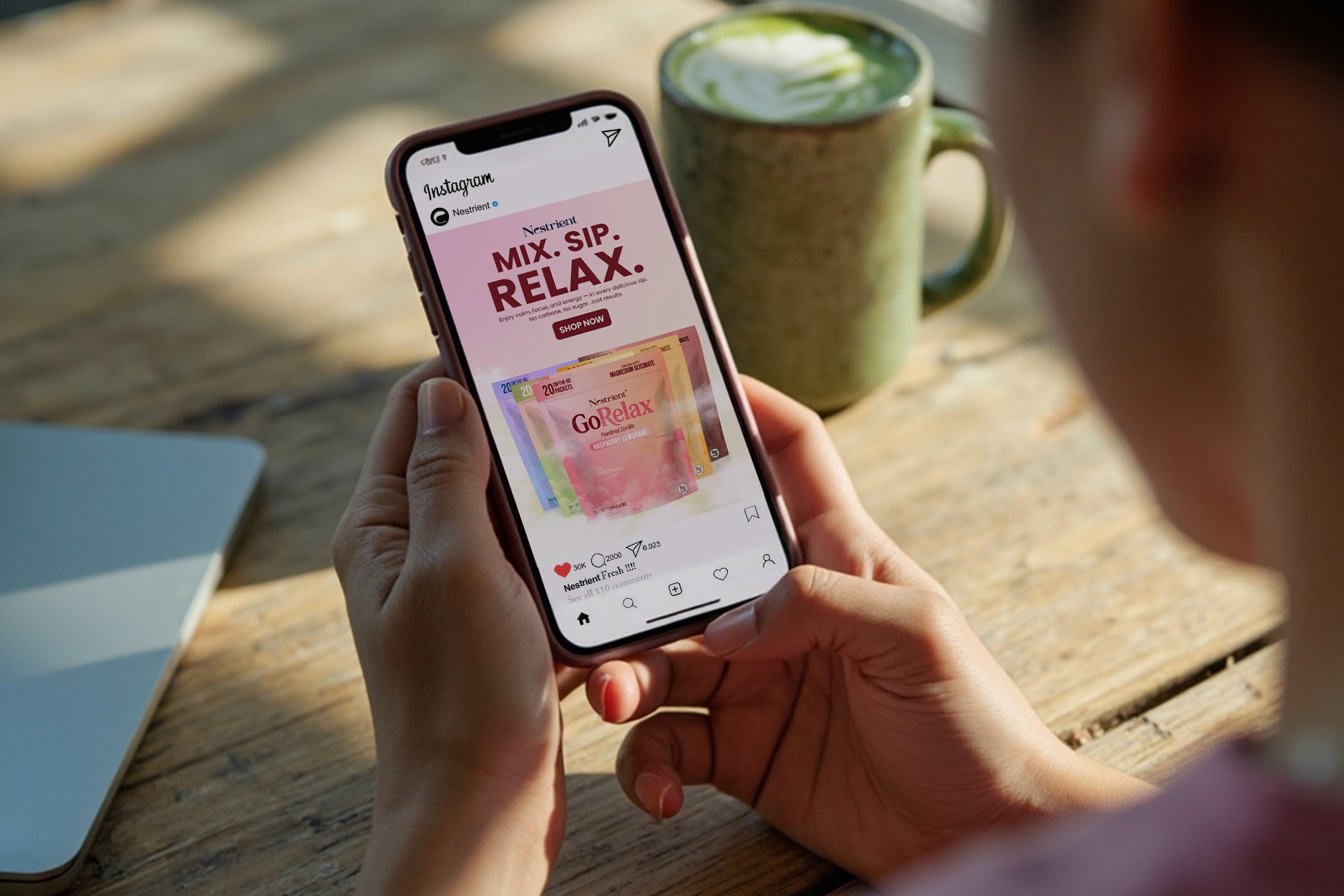 Person holding a smartphone with a tea brand app open, next to a cup of tea on a wooden table.