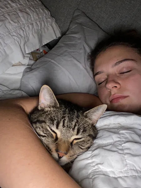 Person sleeping with a cat on their chest in bed