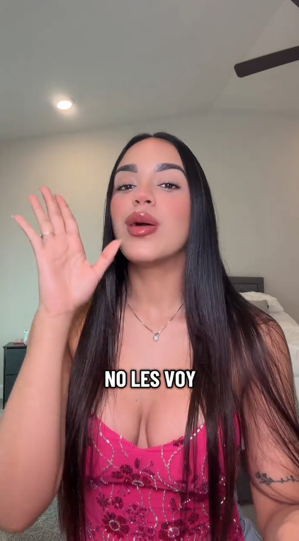 Woman in a pink top with text 'NO LES VOV' waving at the camera.