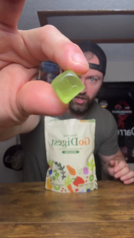 Hand holding a green gummy bear with a 'Go Digest' package in the background