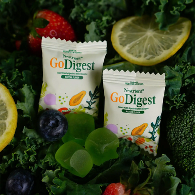 Two packets of N-Struent GoDigest on a bed of greens with fruits and vegetables.